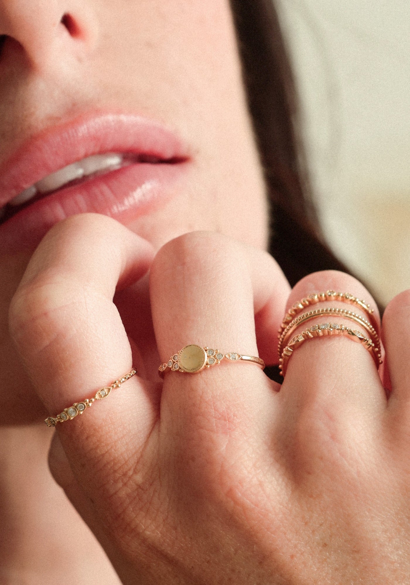 La femme porte la bague Susie Small en or jaune de chez Angèle Brousse tout en posant les doigts sur son menton.