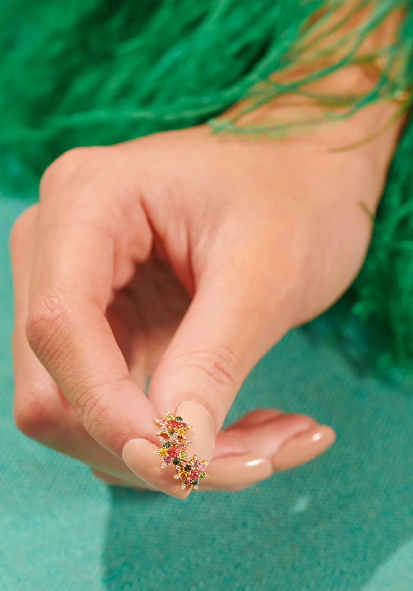 La femme tient entre ses doigts la boucle d'oreille puce en or jaune Arcoiris de chez Rosa Maïtea