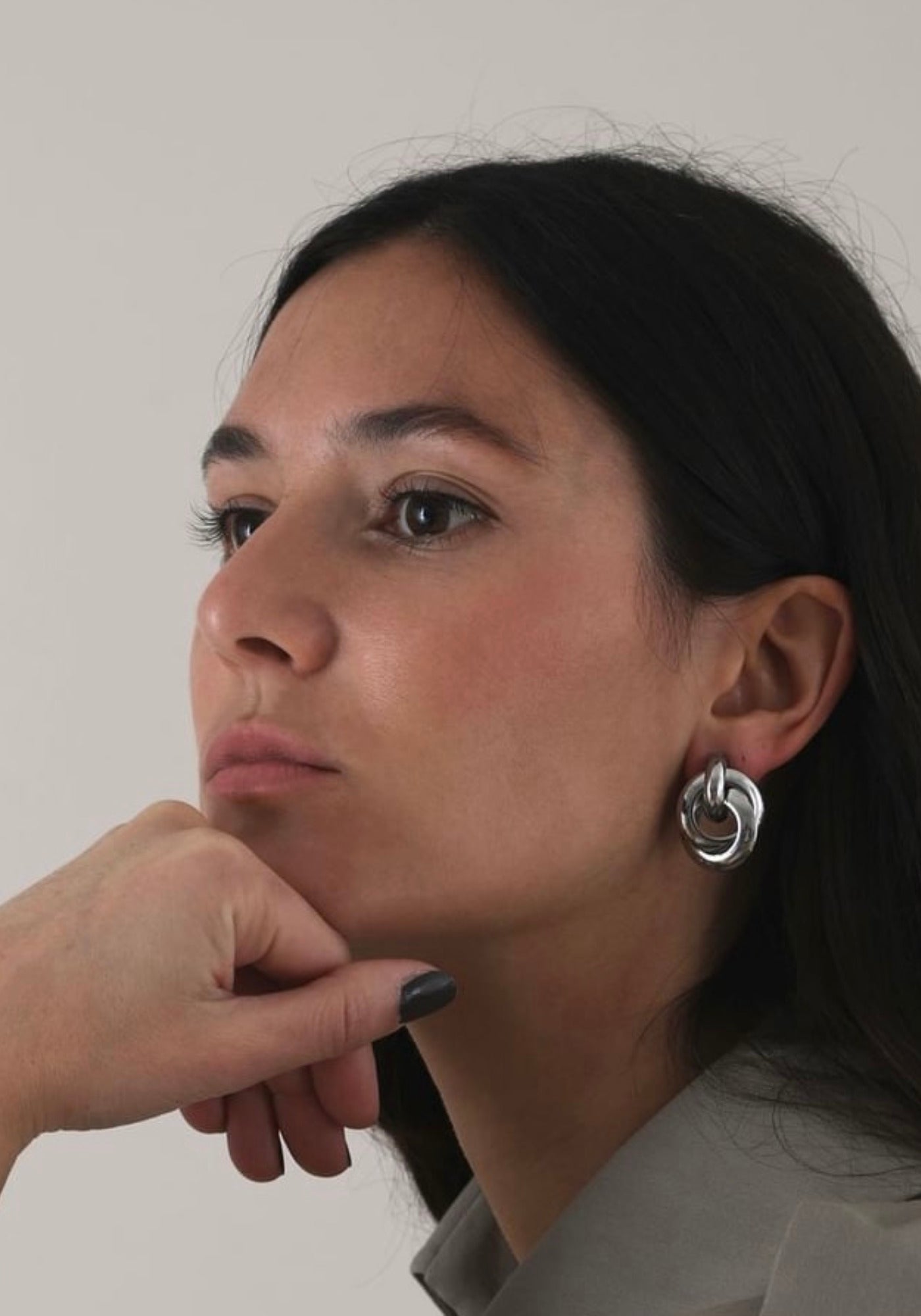 La femme a la main sous le menton et regarde ailleurs en portant les boucles d'oreilles à clip Liz de chez Caprice Paris