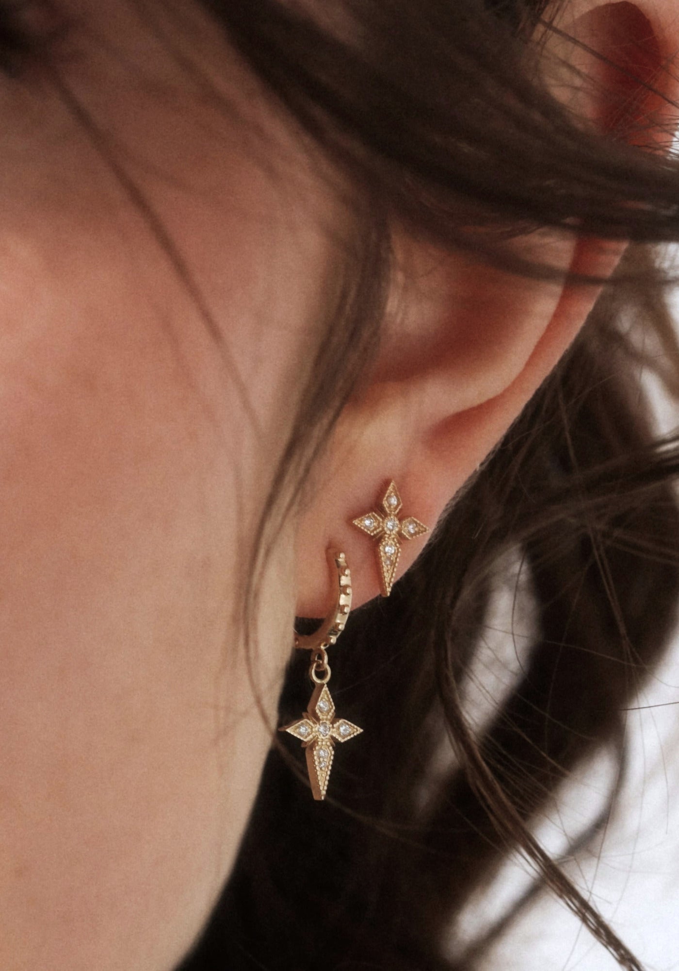 La femme porte la boucle d'oreilles puce croix saintes en or jaune de chez Angèle Brousse