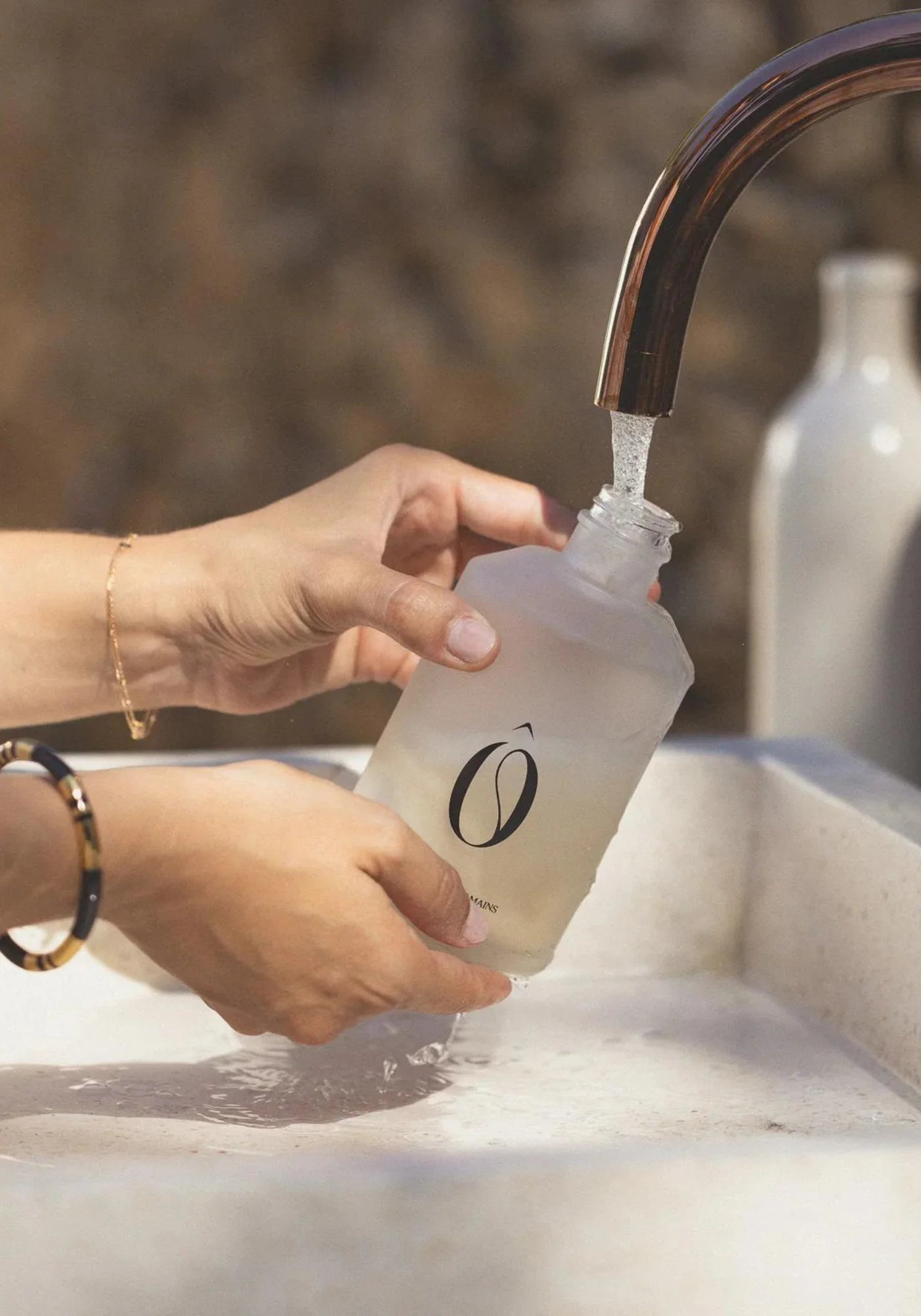 La femme verse l'eau du robinet dans le flacon en verre du coffret signature Terre Salée de chez Fôme