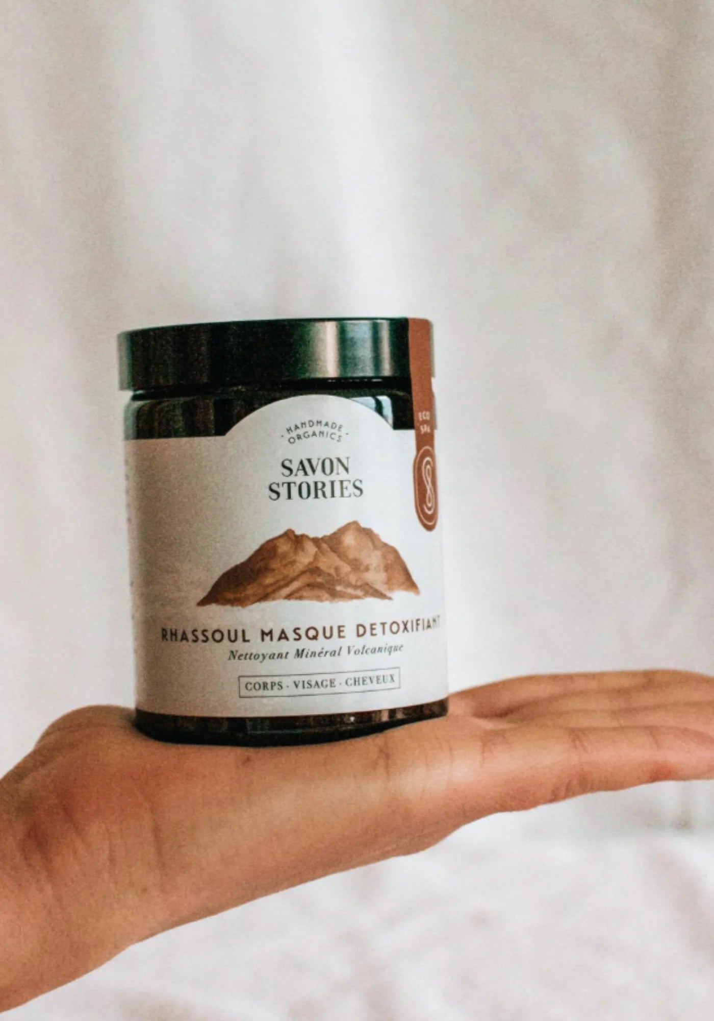 La femme tient dans sa main le masque détoxifiant argile de rhassoul de chez Savon Stories