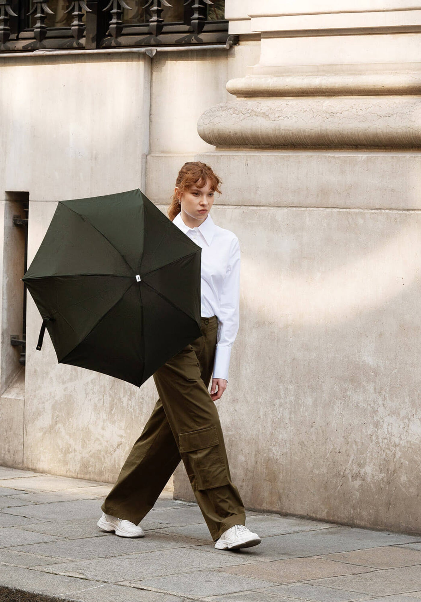 La femme porte, en marchant, le parapluie Léonard kaki de chez Anatole