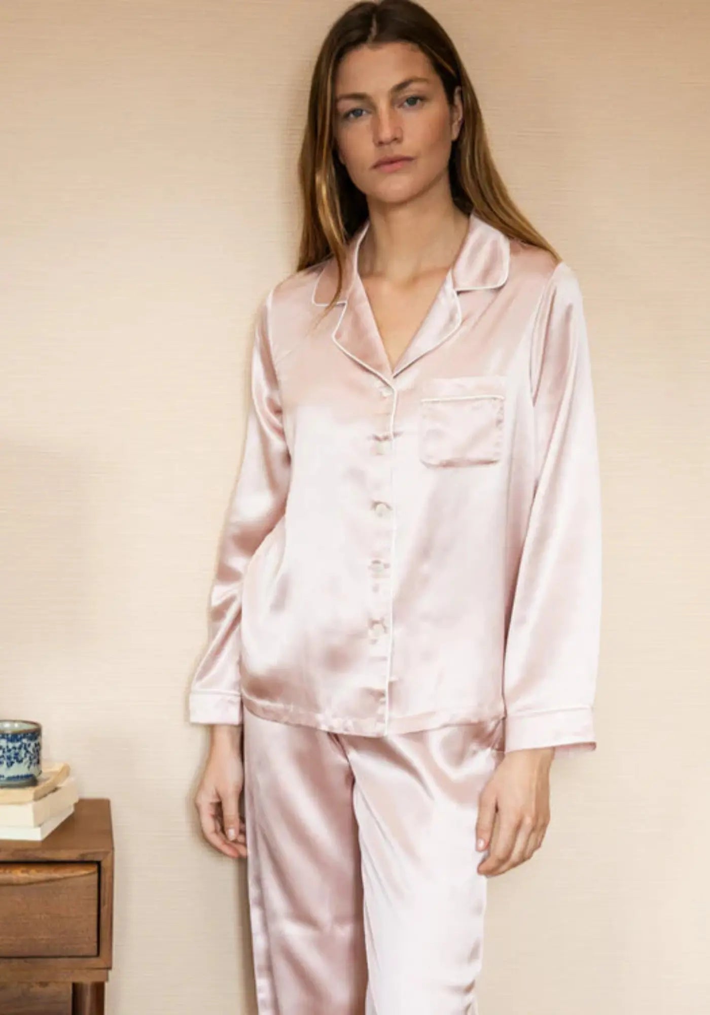 La femme porte le pyjama en soie rose de chez Emily's Pillow
