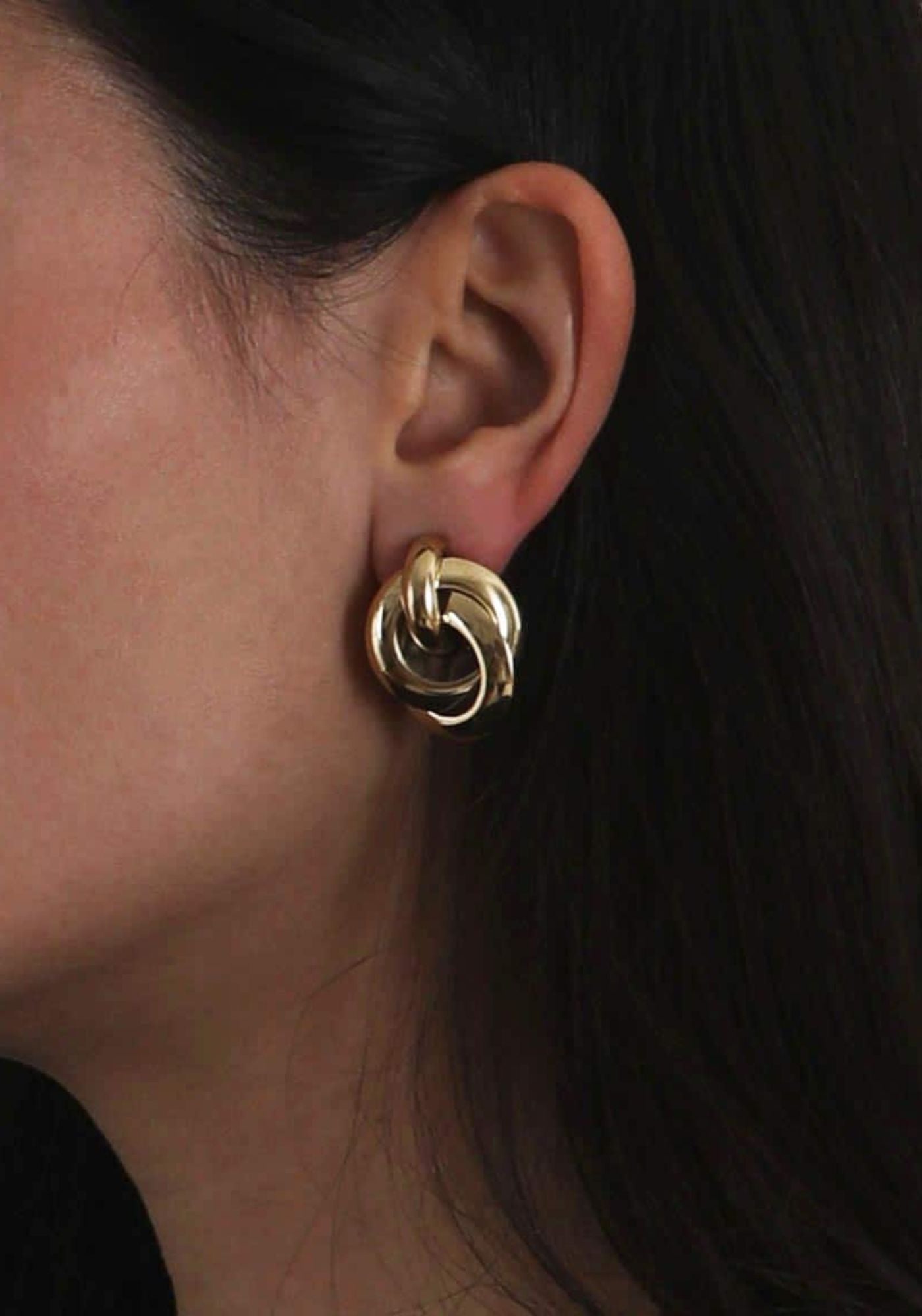 La femme porte les boucles d'oreilles créoles torsadées dorées LIz de chez Caprice Paris