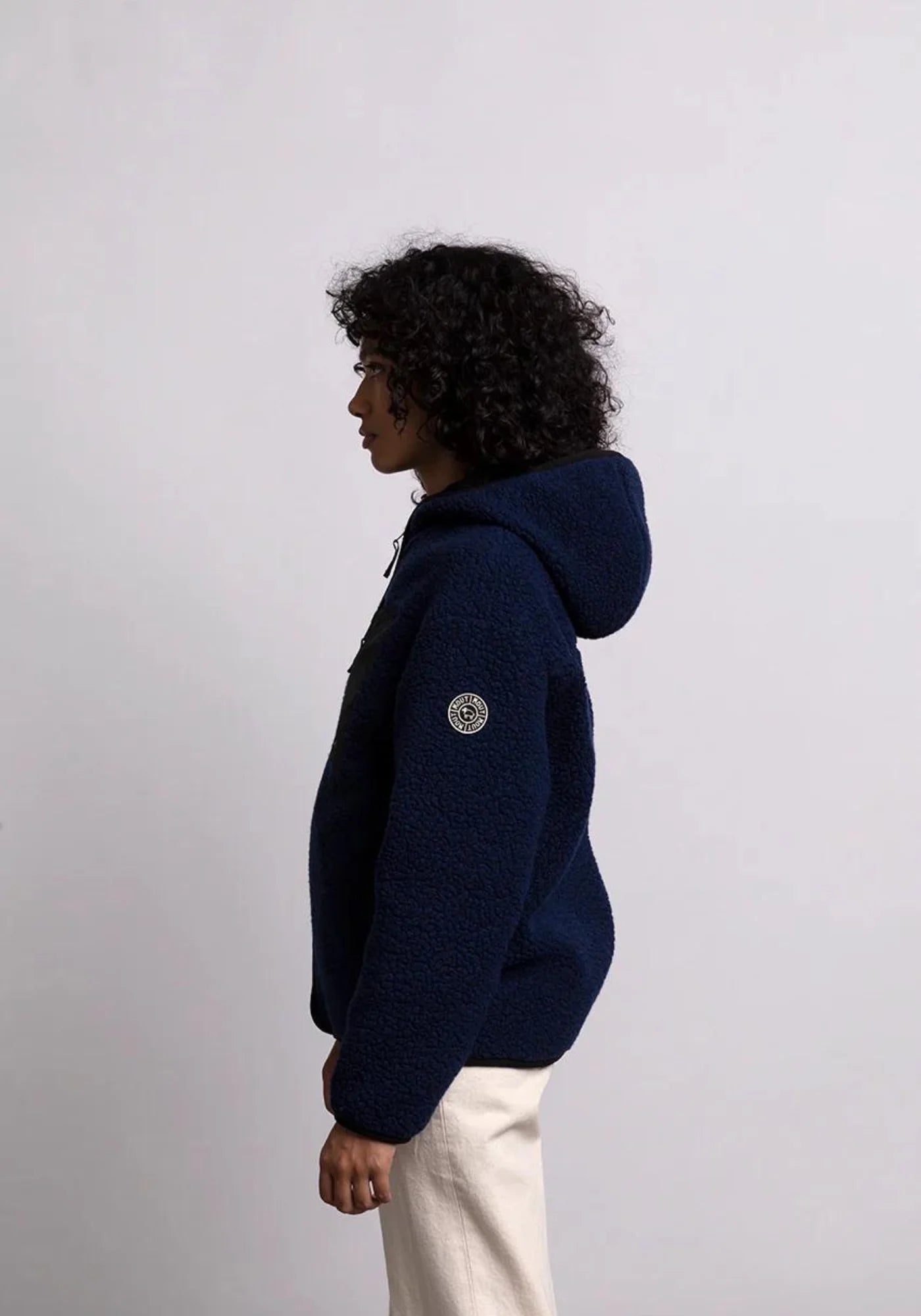 la femme est de coté et porte la veste sherpa unisexe hood bleu marine de chez mout mout 