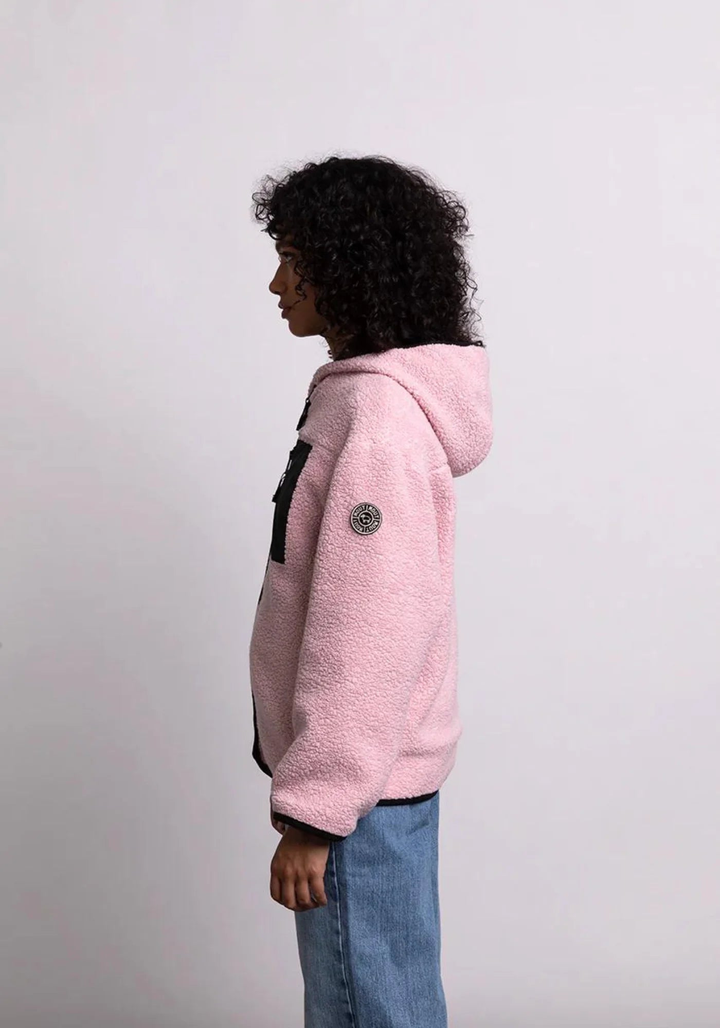 la femme est de coté et porte la veste sherpa unisexe hood rose cde chez mout mout 