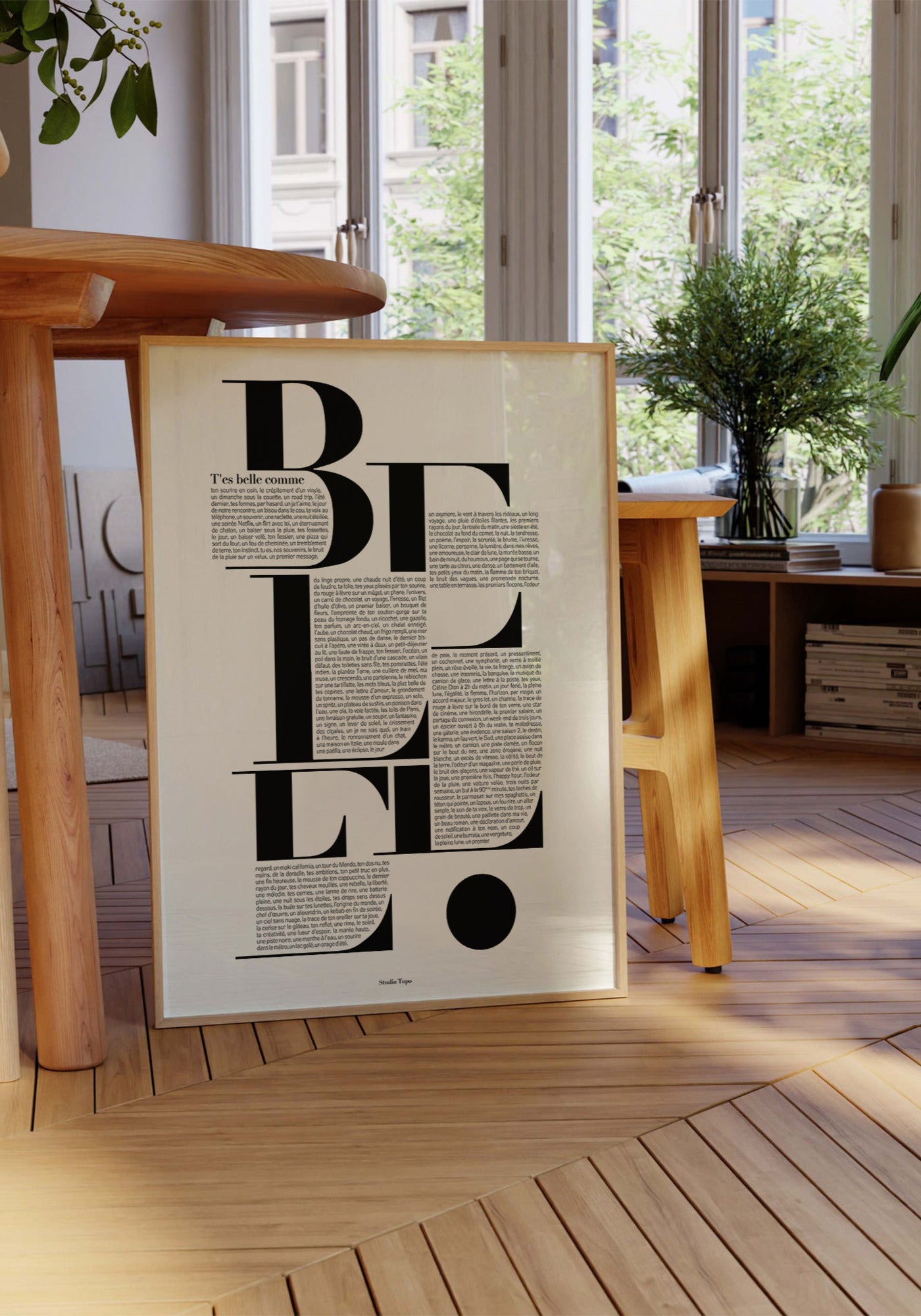 L'affiche typographique "T'es belle comme" en 30x40 cm de chez Studio Topo posée au sol contre une table et un tabouret en bois