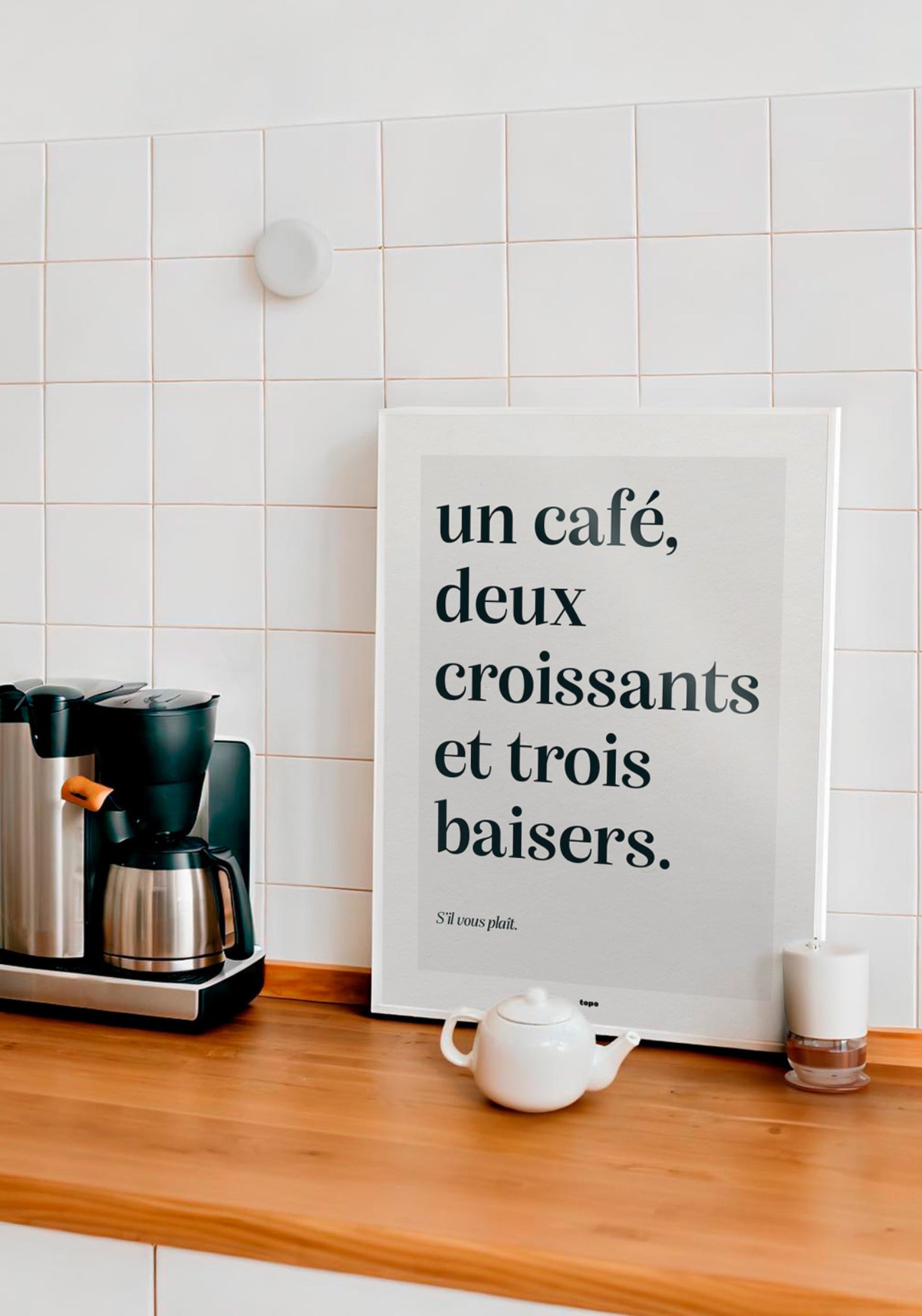 L'affiche typographique "Un café, deux croissants et trois baisers" en 21x30 cm et 30x40 cm de chez Studio Topo posée sur un plan de travail