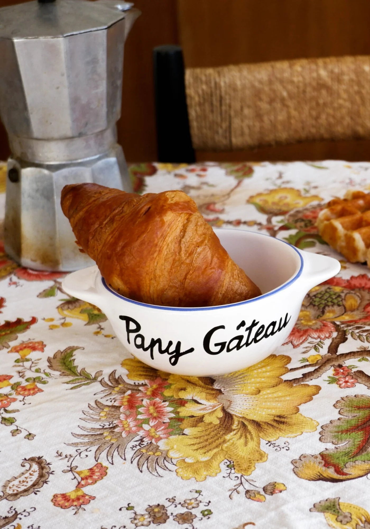 Le bol breton en faïence Papy Gâteau de chez Pied de Poule posé sur une vielle nappe et un croissant dedans