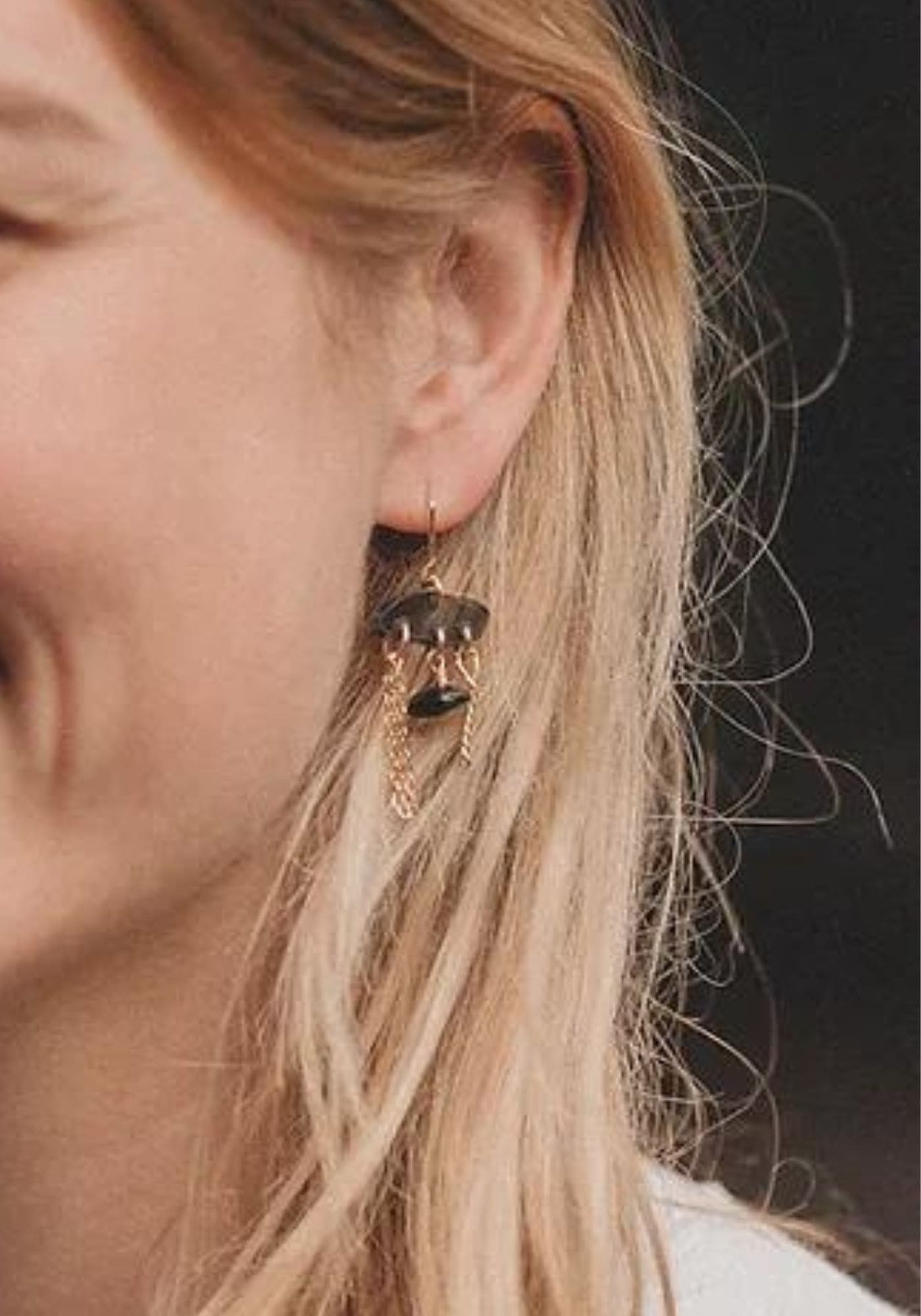 La femme porte les boucles d'oreilles Charlie en couleur noire de chez Anna Shelley