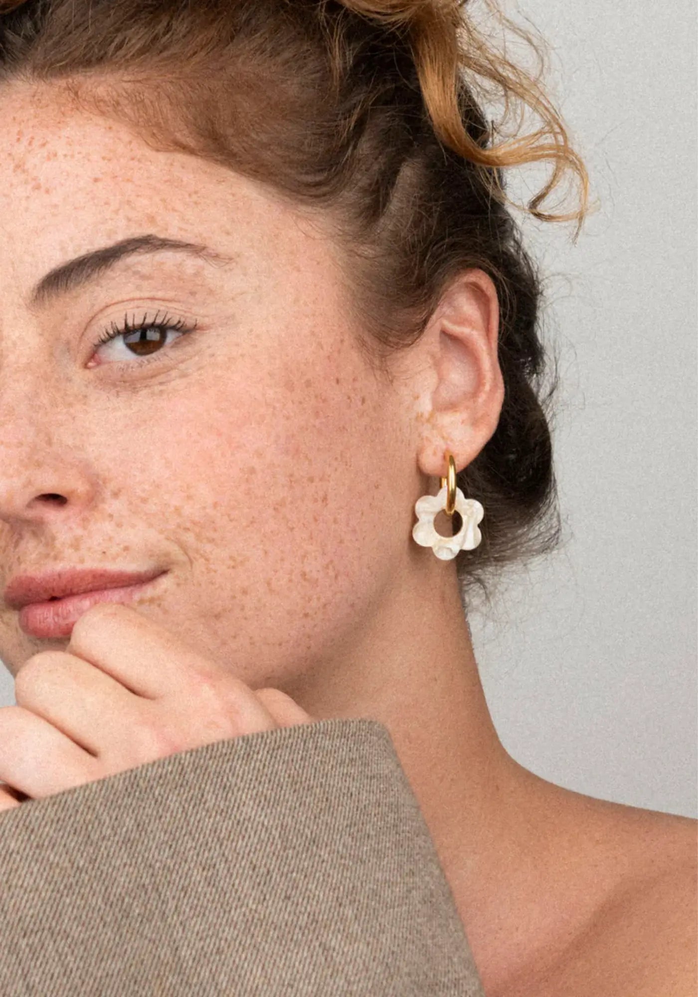 La femme porte les boucles d'oreilles fleurette nude baby de chez Kurage Ginza