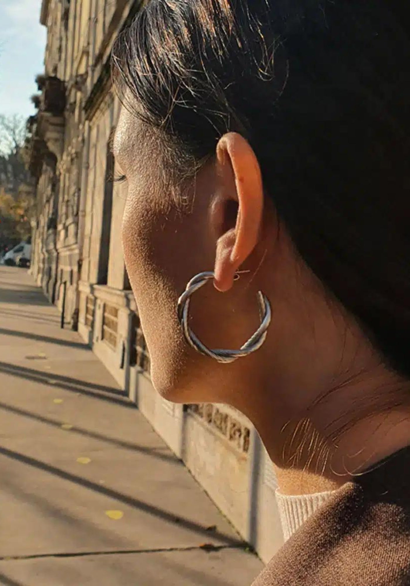 La femme porte les boucles d'oreilles Déméter en argent de chez Caprice Paris 