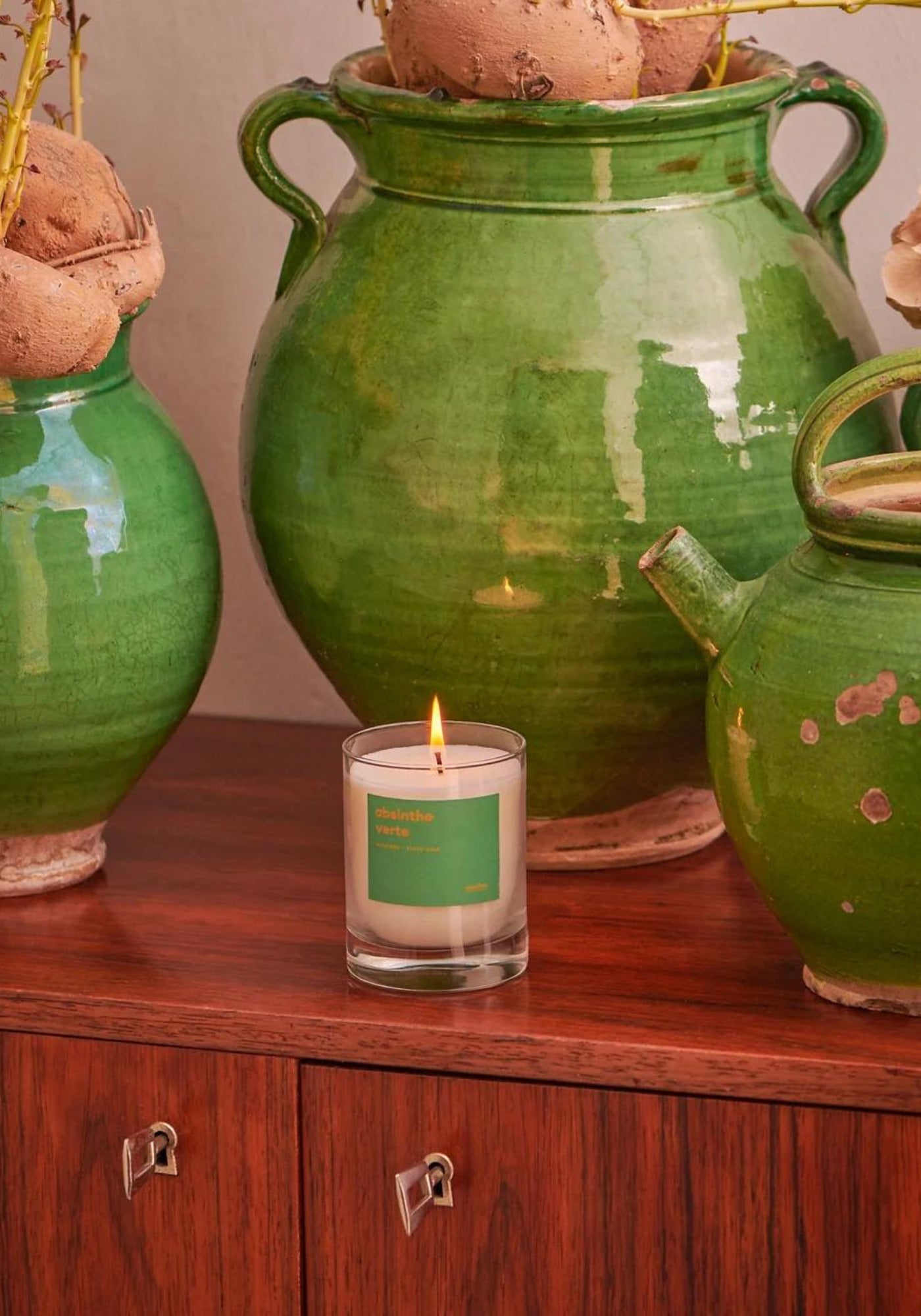 La bougie parfumée Absinthe verte de chez Récoltes est allumée et posée sur un meuble