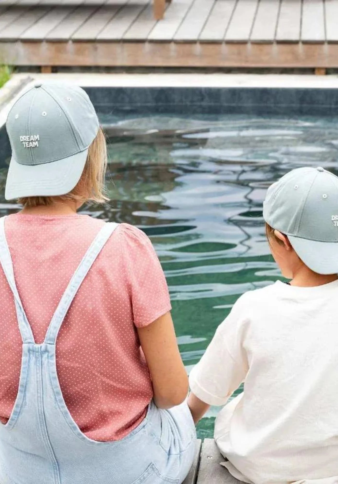 Une mère et son fil assis au bord de la piscine portent la casquette Dream Team pour enfant et adulte de chez Chamaye