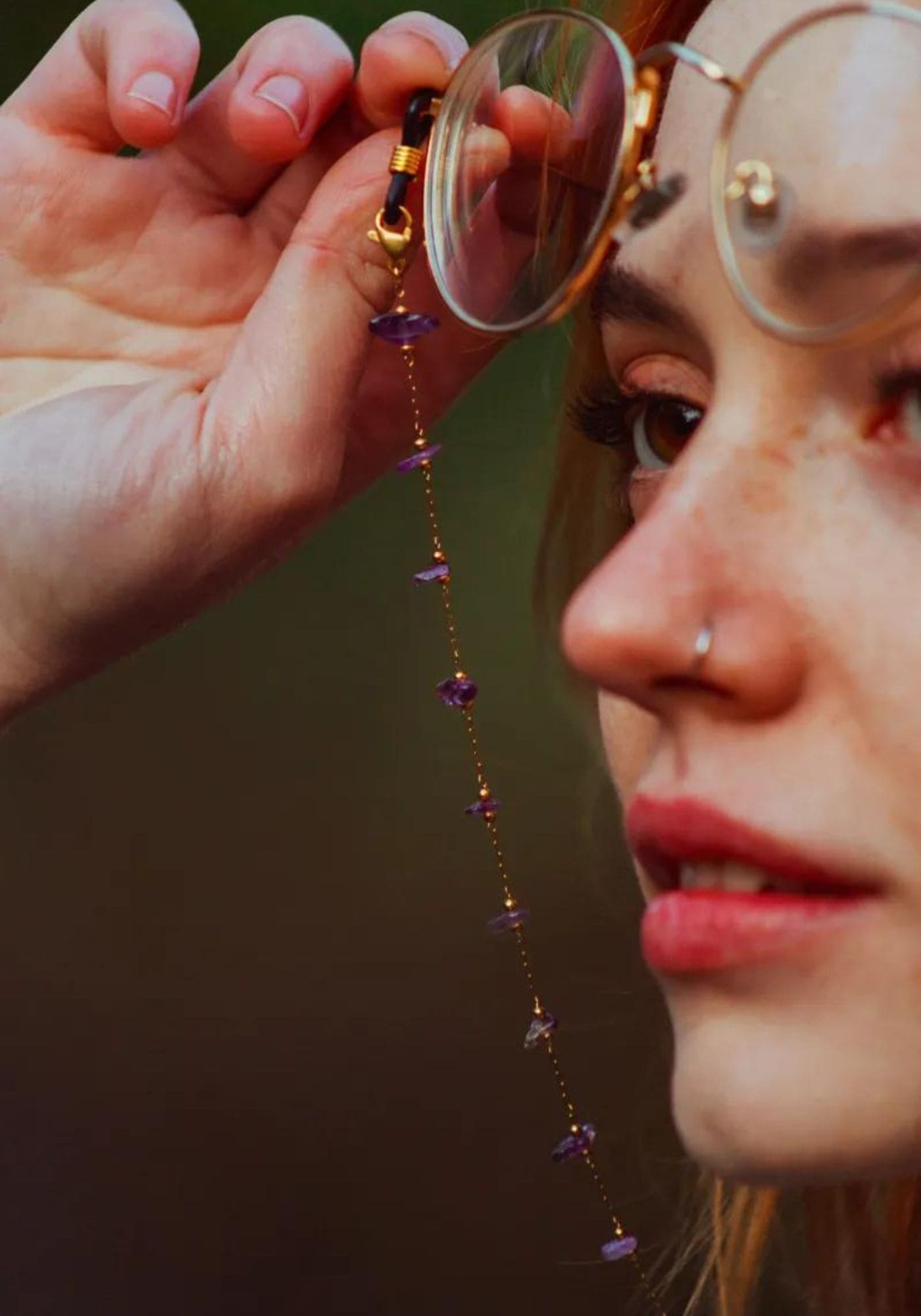 La femme regarde l'horizon en tenant à la main des lunettes de vue avec la chaîne de lunettes Aurore de chez Atelier Kat H