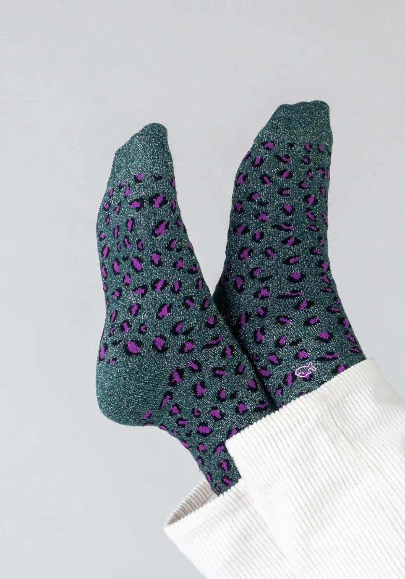 La femme a les jambes en l'air et croisées. Elle porte les chaussettes à motif léopard vert et violet de chez Billybelt