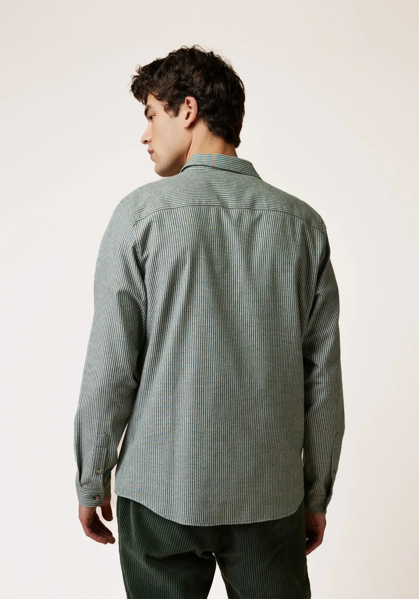 L'homme est de dos et porte la chemise Iraty rayé vert et écru de chez Faguo