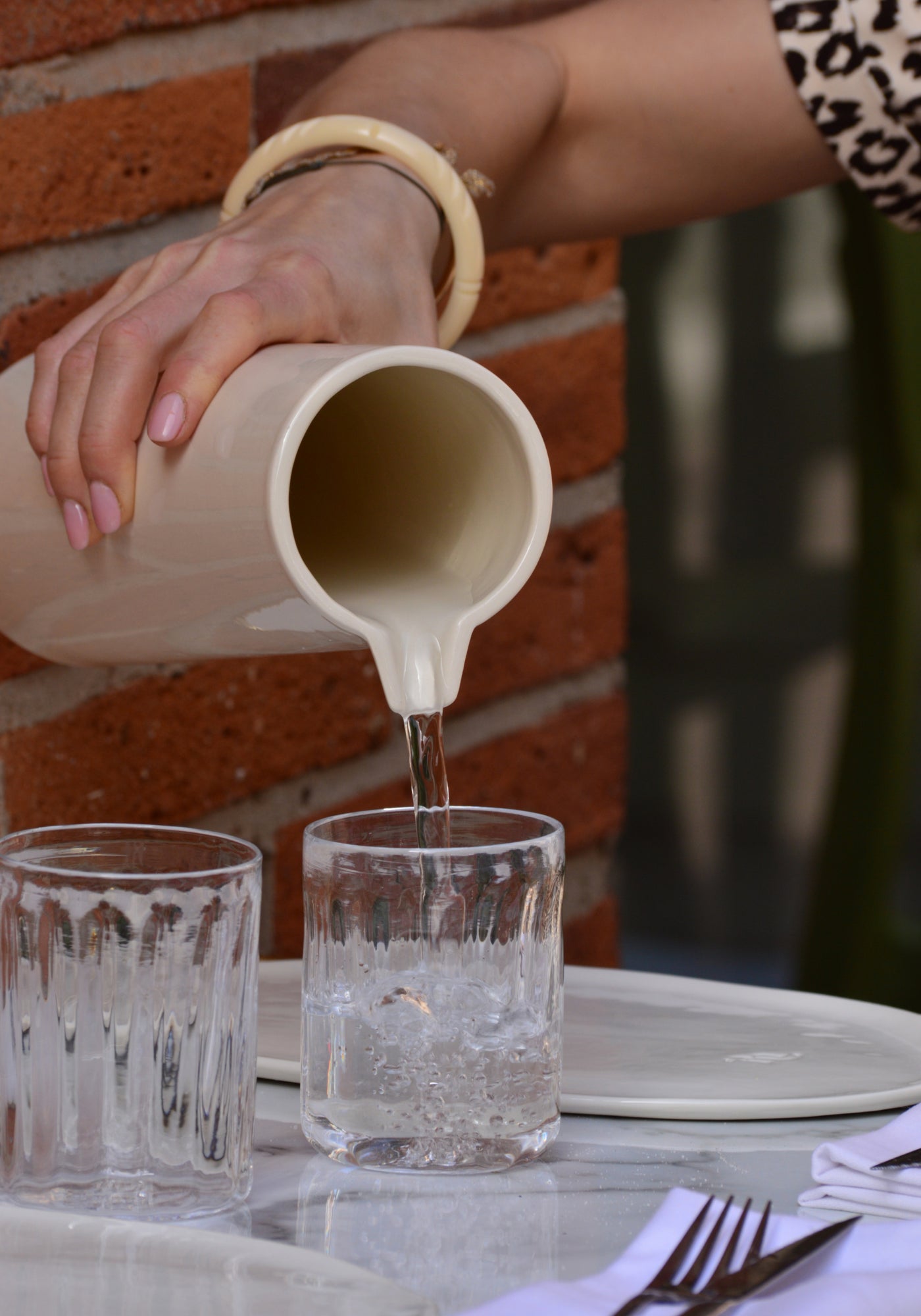 La femme verse dans un verre de l'eau avec le grand pichet en Grès beige de chez Maison Marah