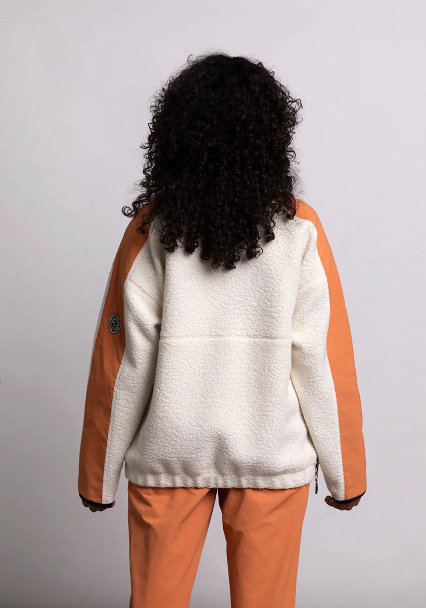 La femme de dos porte le hoodie Sherpa unisexe Cocoon écrue et orange de chez Mout Mout