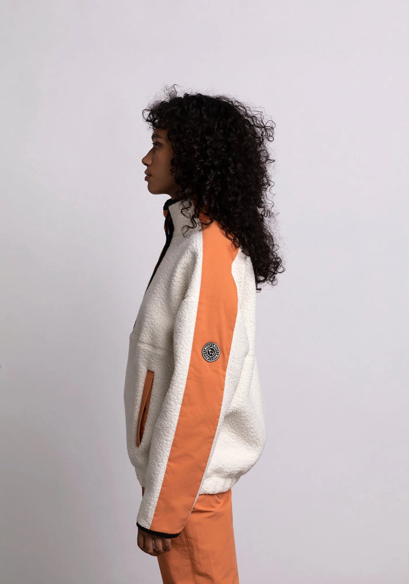 La femme de profil porte le hoodie Sherpa unisexe Cocoon écrue et orange de chez Mout Mout