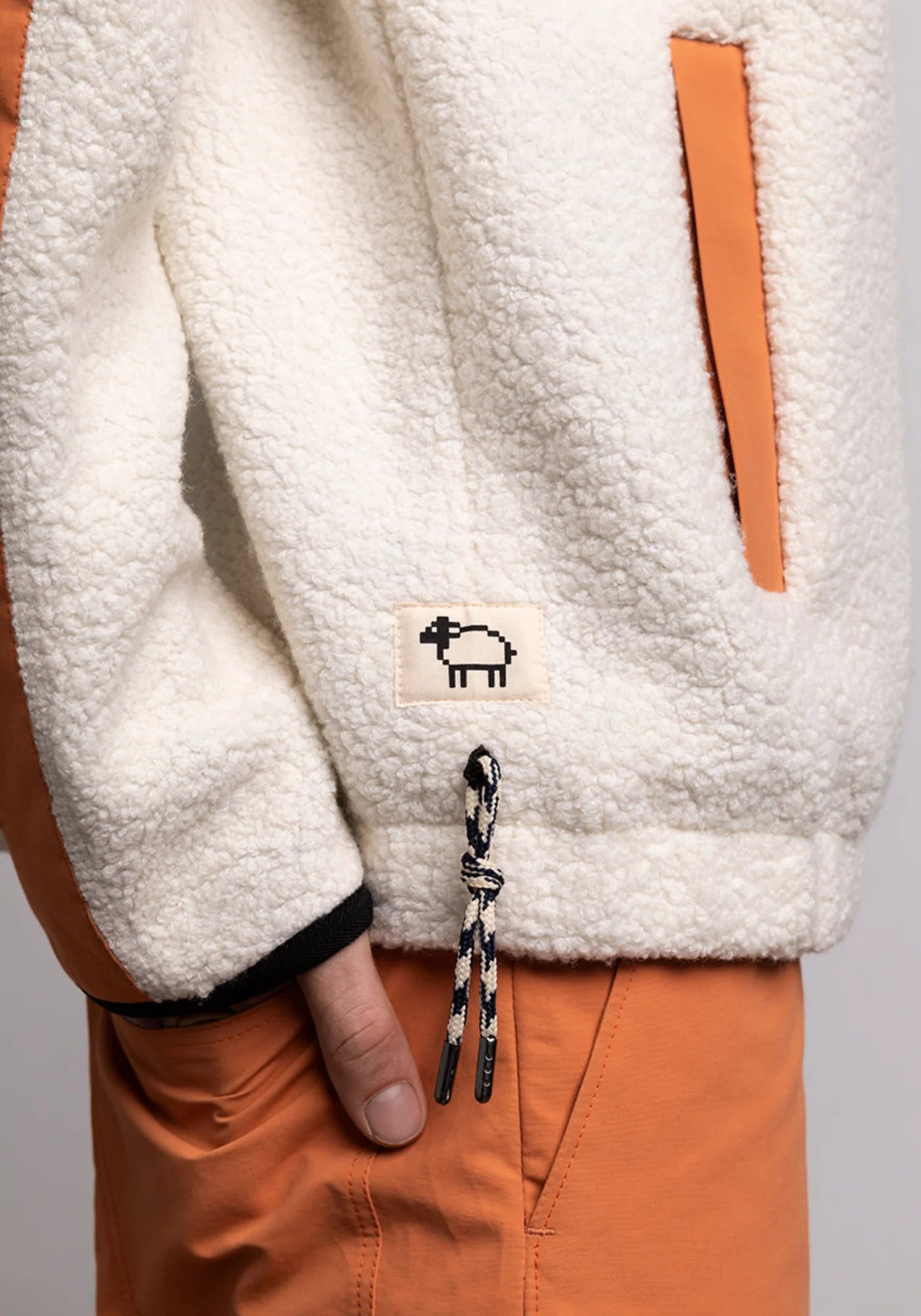 Zoom sur le logo et l'élastique sur le côté droit du hoodie Sherpa unisexe Cocoon écrue et orange de chez Mout Mout