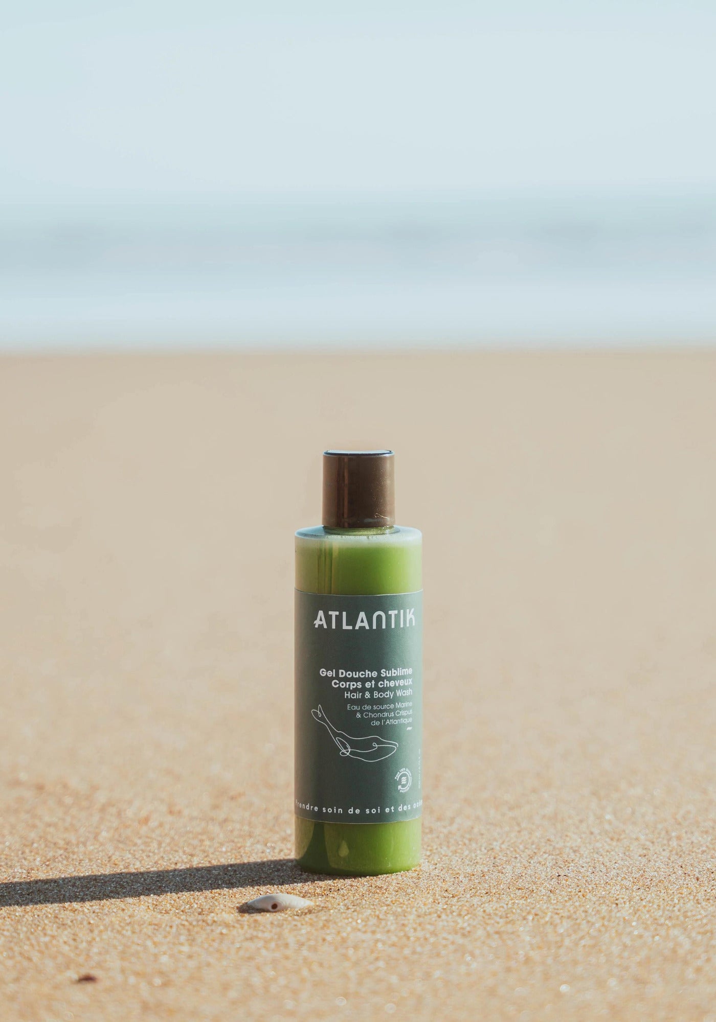 Le gel douche corps et cheveux sublime de chez Atlantik Care posé sur une plage