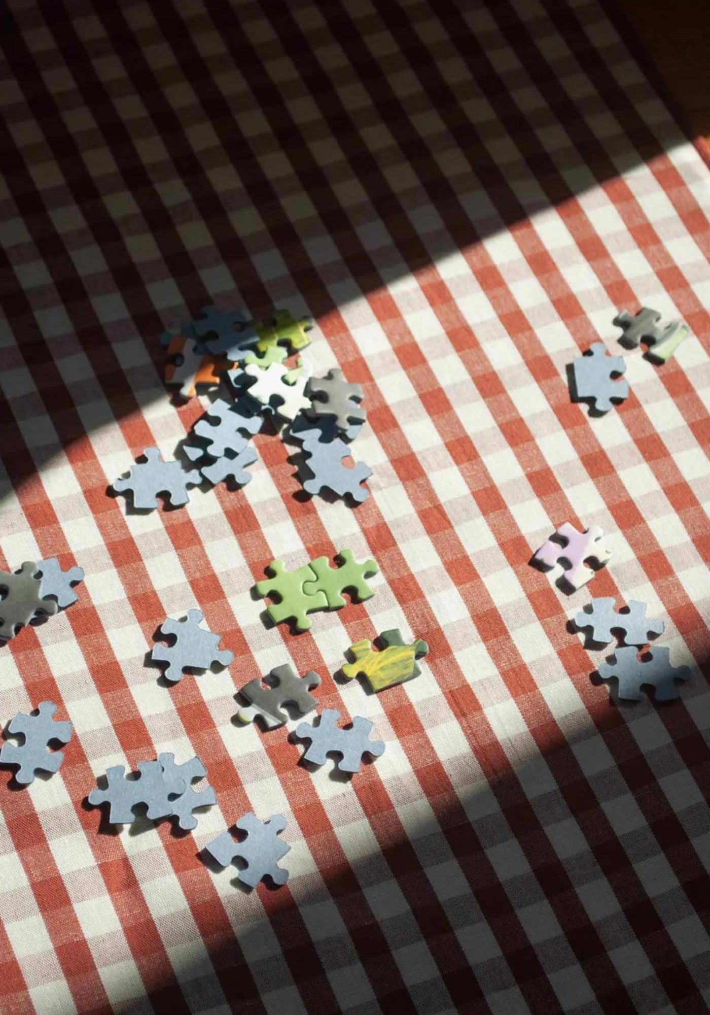 Zoom sur le vichy de la nappe en lin et coton rouille de chez Les Pensionnaires accompagnée de pièces de puzzle