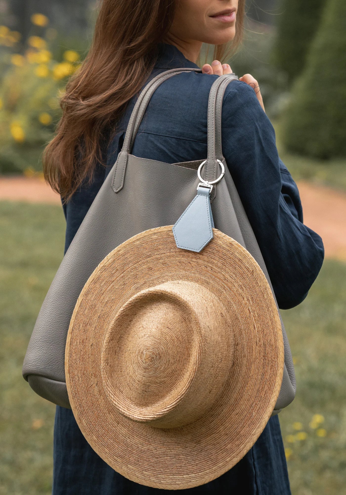 La femme porte un sac sur sur épaule. Accrochée au sac et au chapeau, la pince à chapeau Cristal bleu clair de chez Palma B