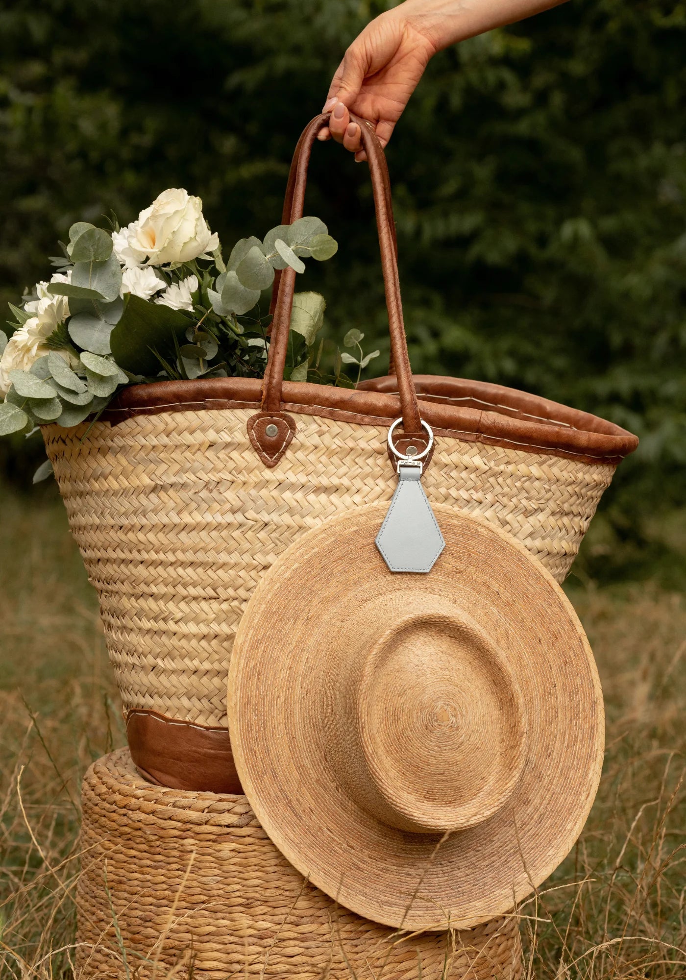 La pince à chapeau Cristal bleu clair de chez Palma B accrochée à un panier et à un chapeau de paille