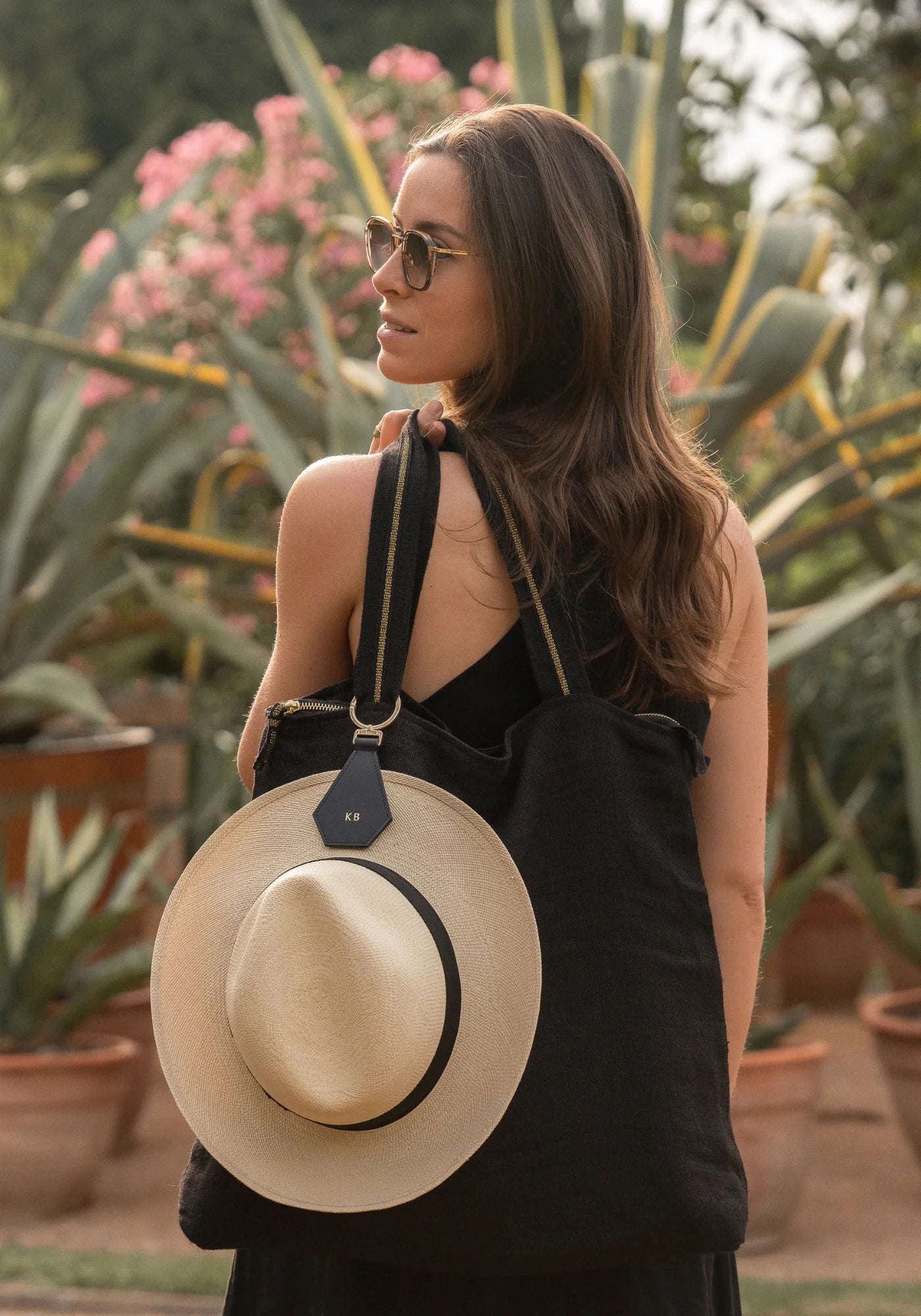 La femme porte un sac sur sur épaule. Accrochée au sac et au chapeau, la pince à chapeau Cristal noir de chez Palma B