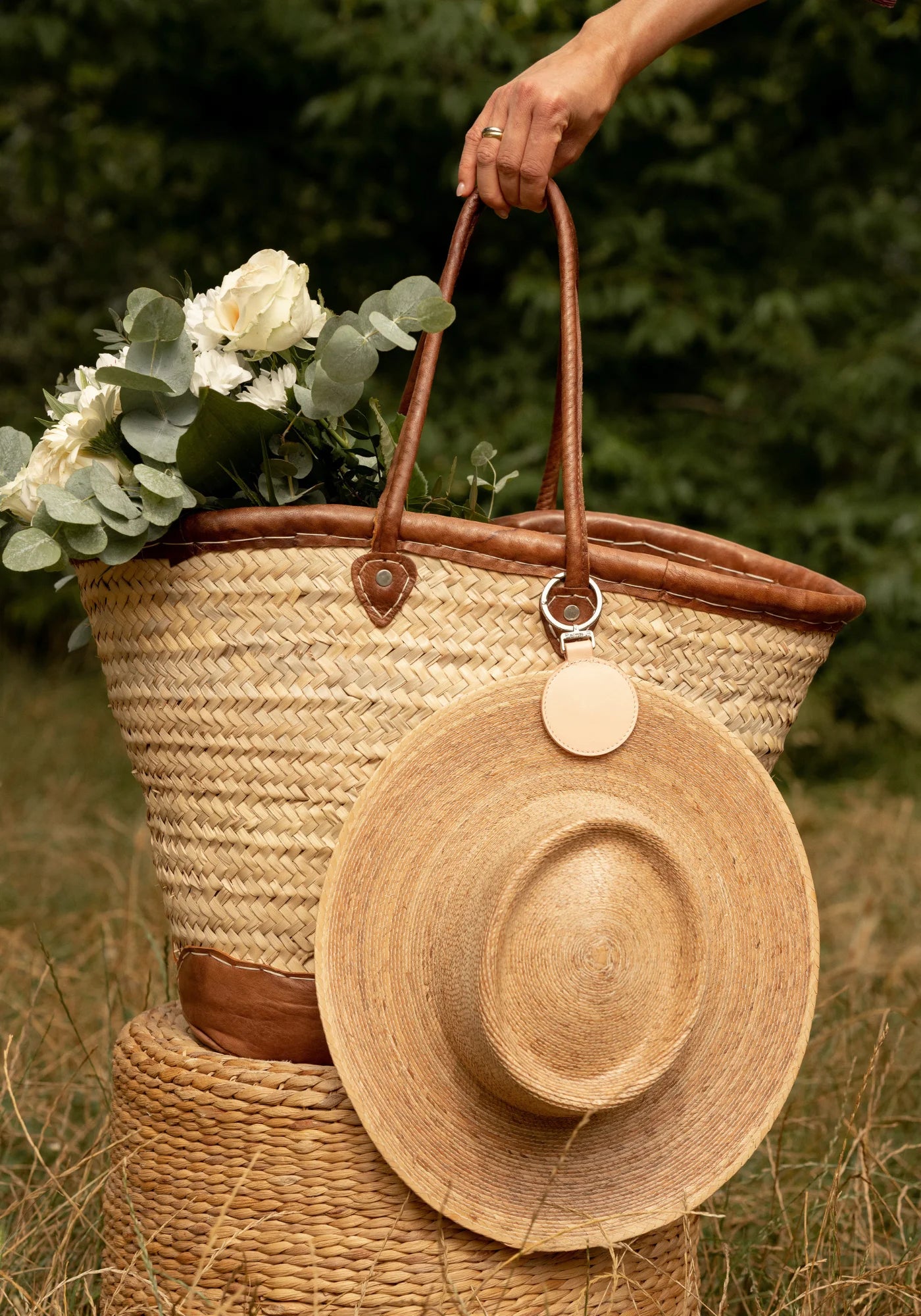 La pince à chapeau Sun rose pâle de chez Palma B accrochée à un panier et à un chapeau de paille