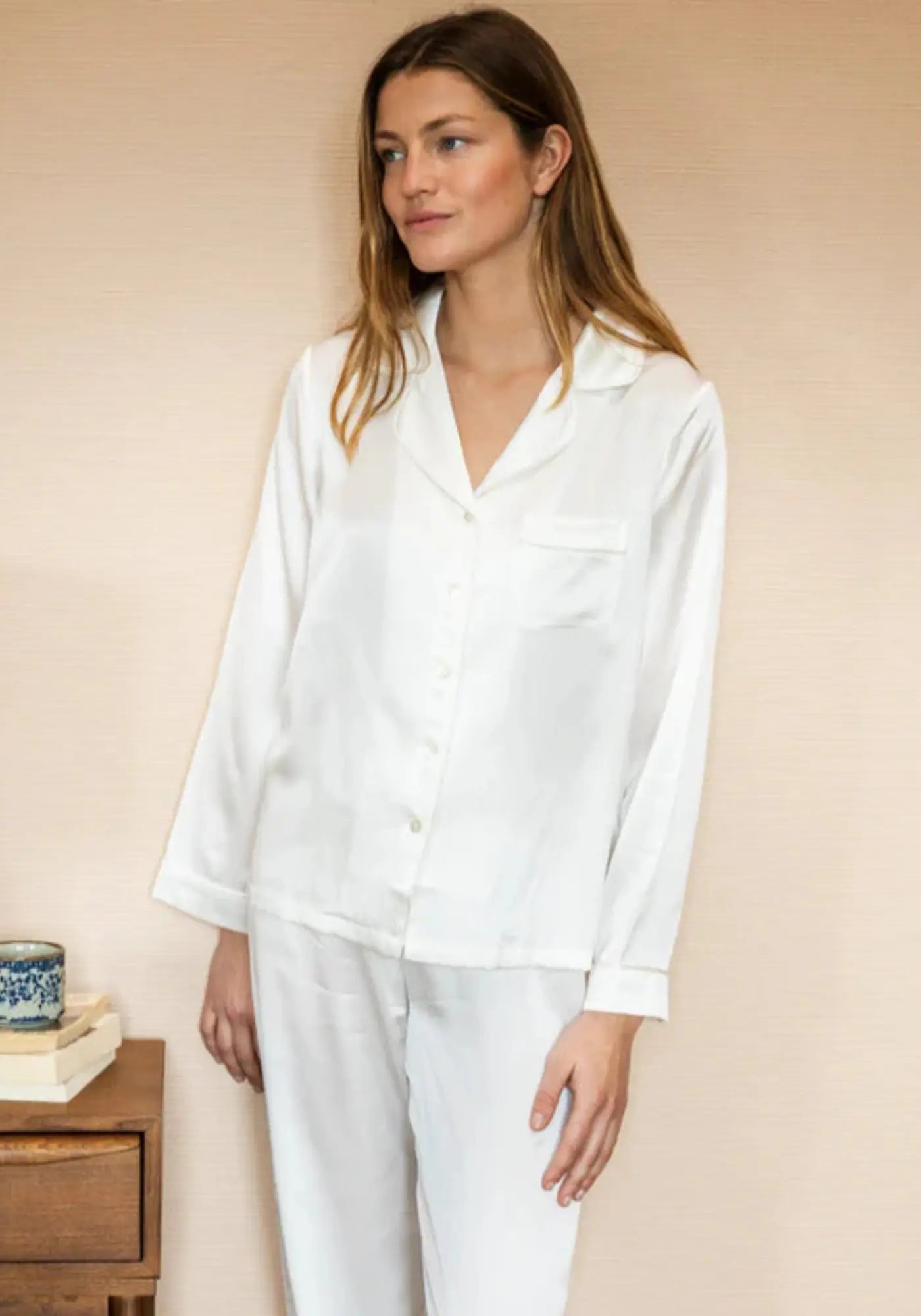 La femme porte le pyjama en soie blanc de chez Emily's Pillow