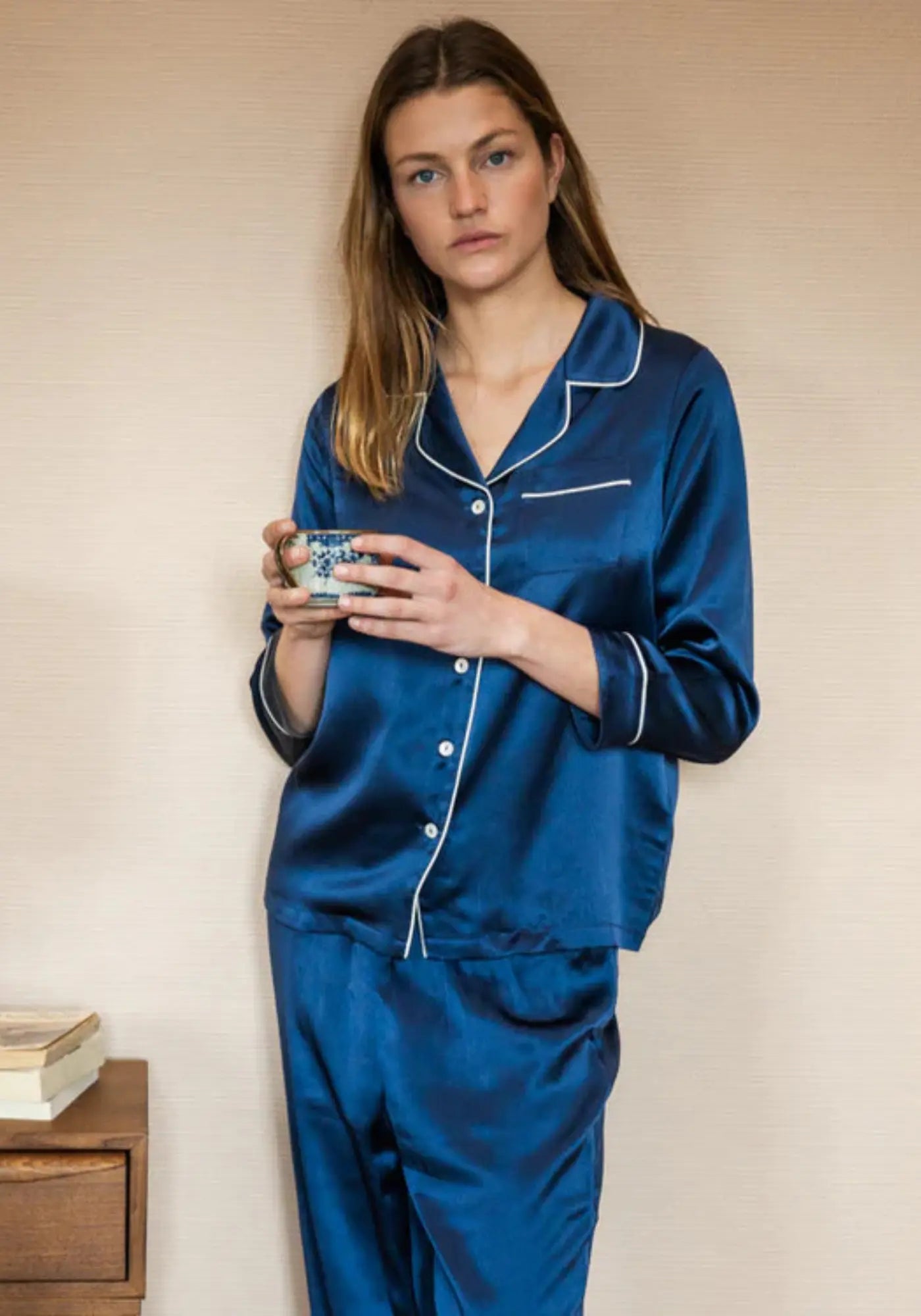 La femme porte le pyjama en soie bleu nuit de chez Emily's Pillow