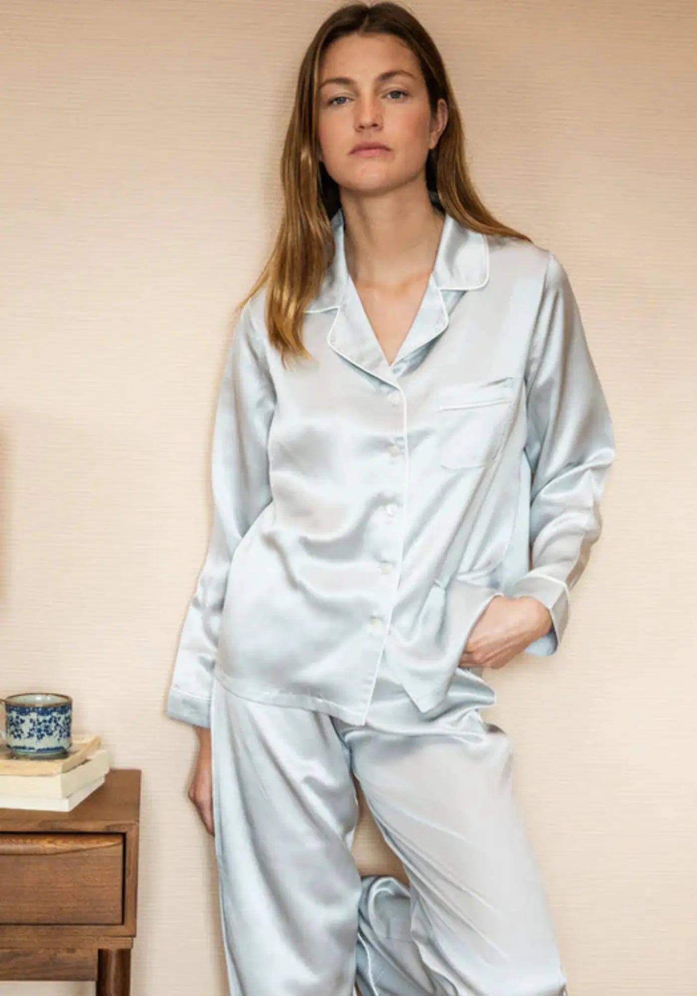 La femme porte le pyjama en soie gris perle de chez Emily's Pillow