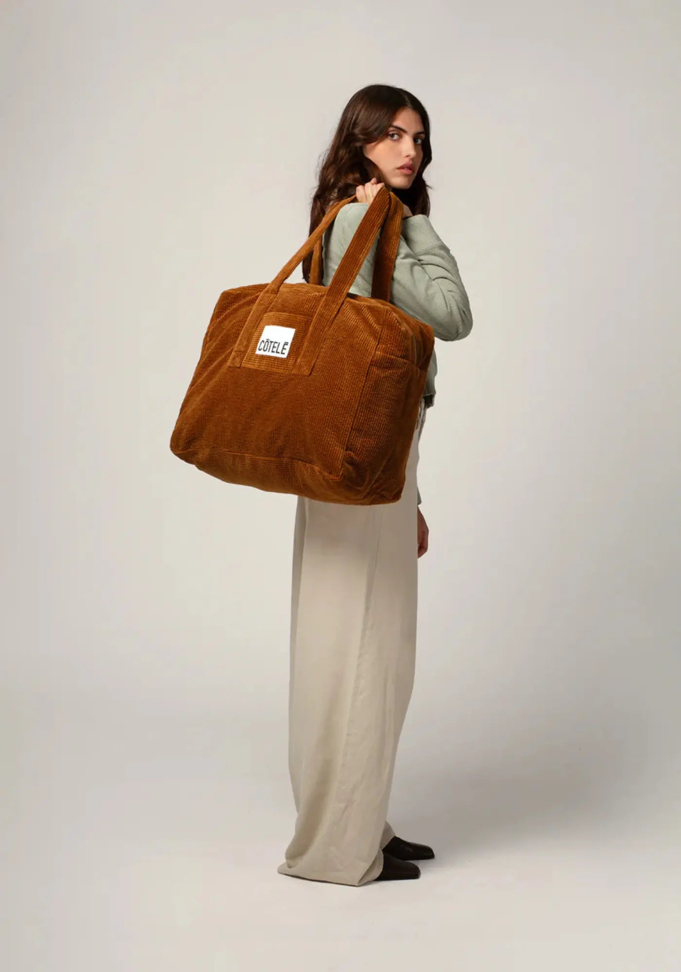 La femme porte le sac en velours week-end Bonny camel de chez Cotelé Paris