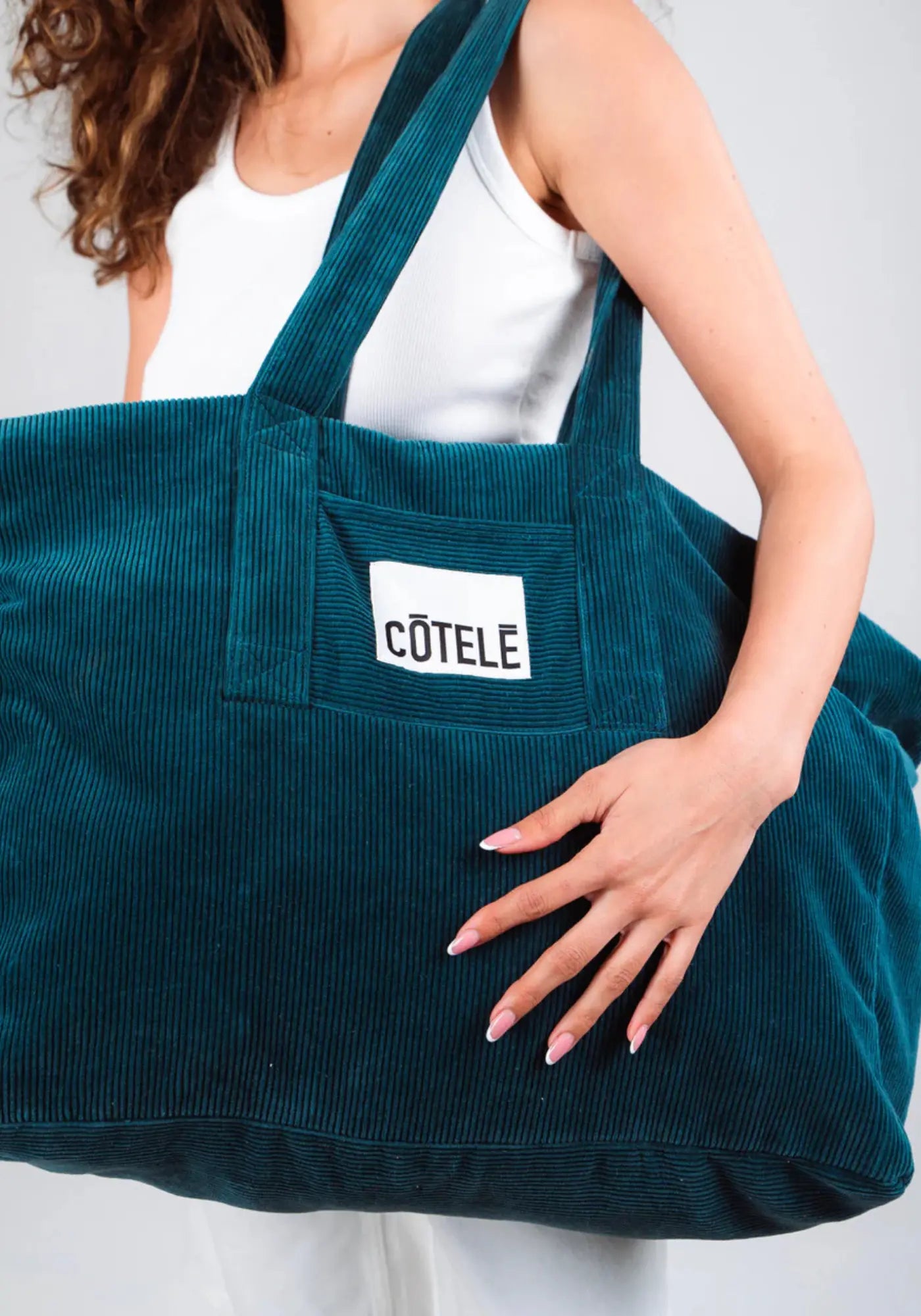 La femme porte le sac en velours week-end Bonny couleur pétrole de chez Côtelé Paris 