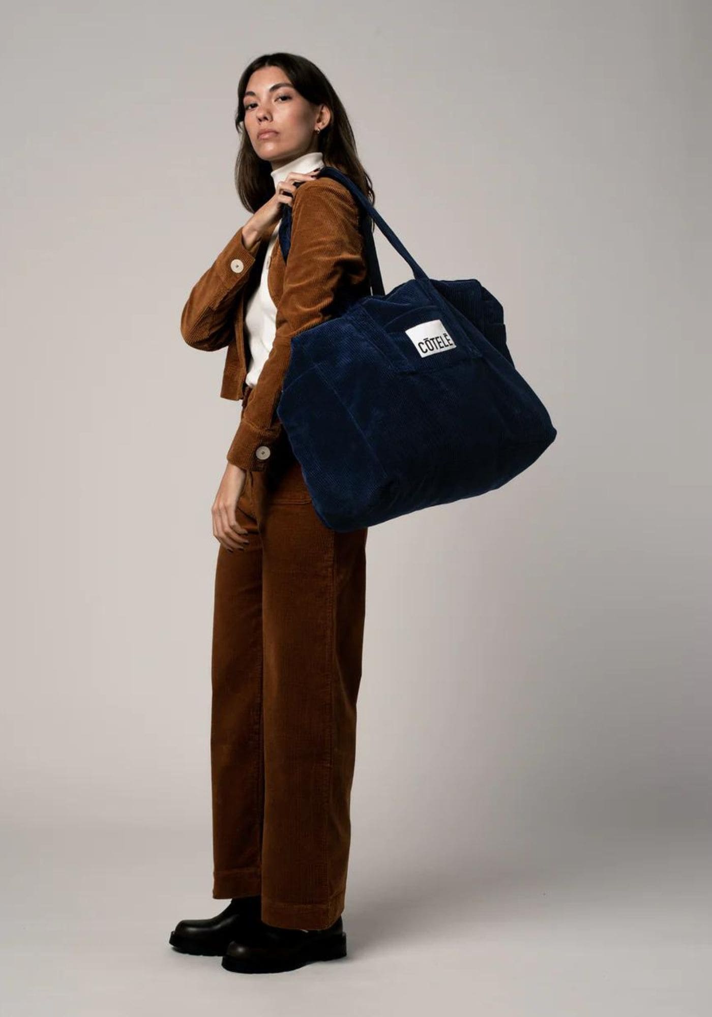 La femme porte à l'épaule  le sac de voyage Bonny en denim bleu de chez Côtelé Paris