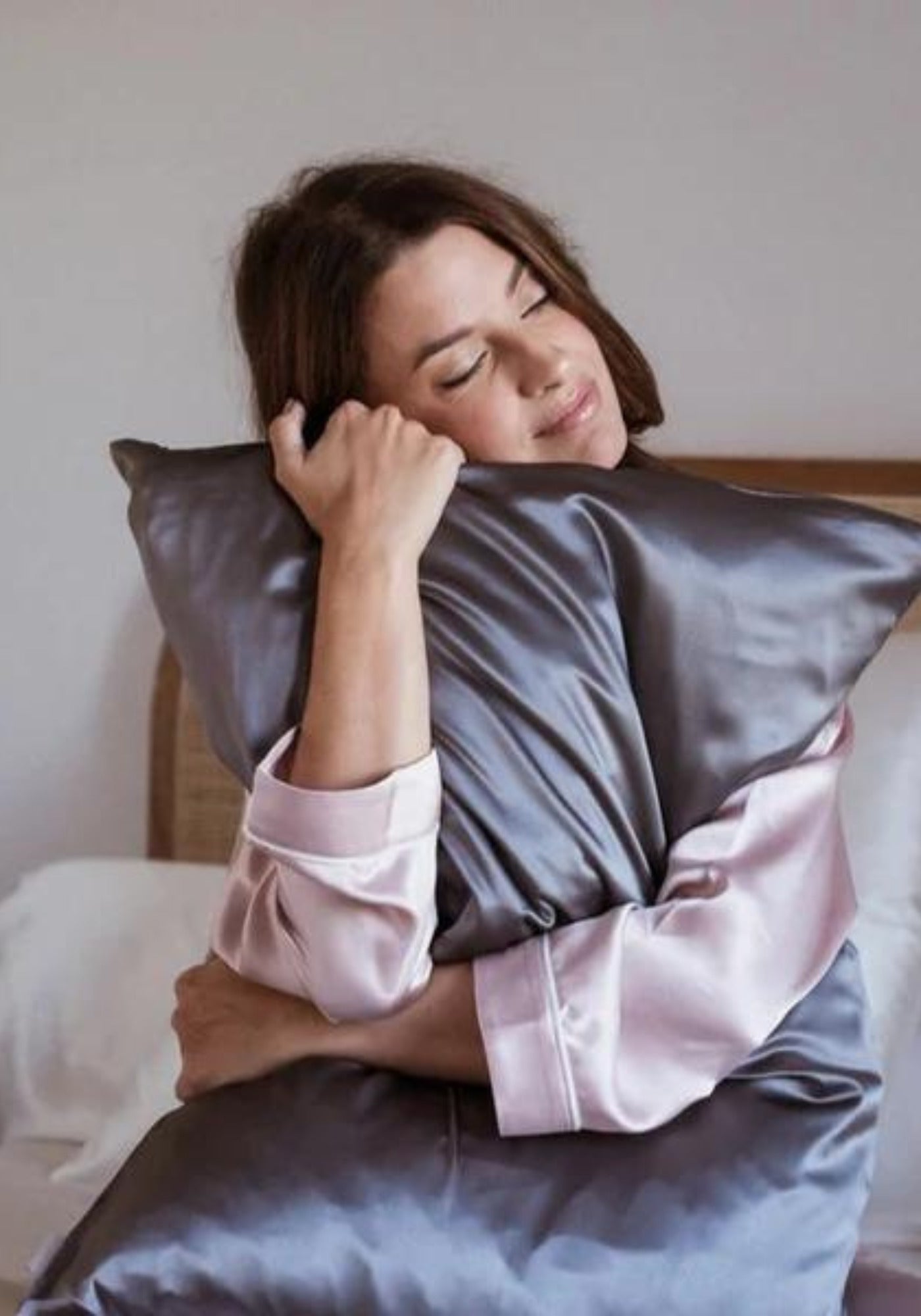 La femme tient contre elle l'oreiller avec la taie en soie gris intense de chez Emily's Pillow