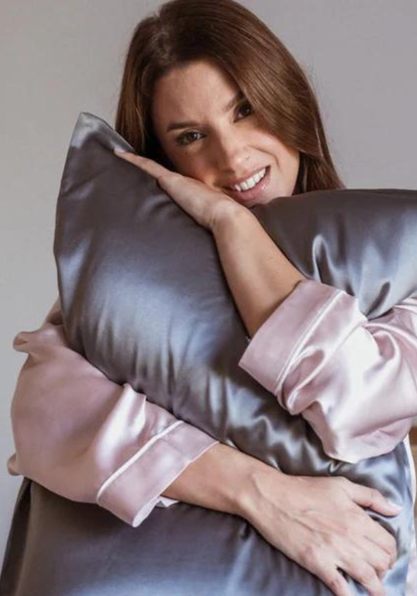 La femme tient contre elle l'oreiller avec la taie en soie gris intense de chez Emily's Pillow