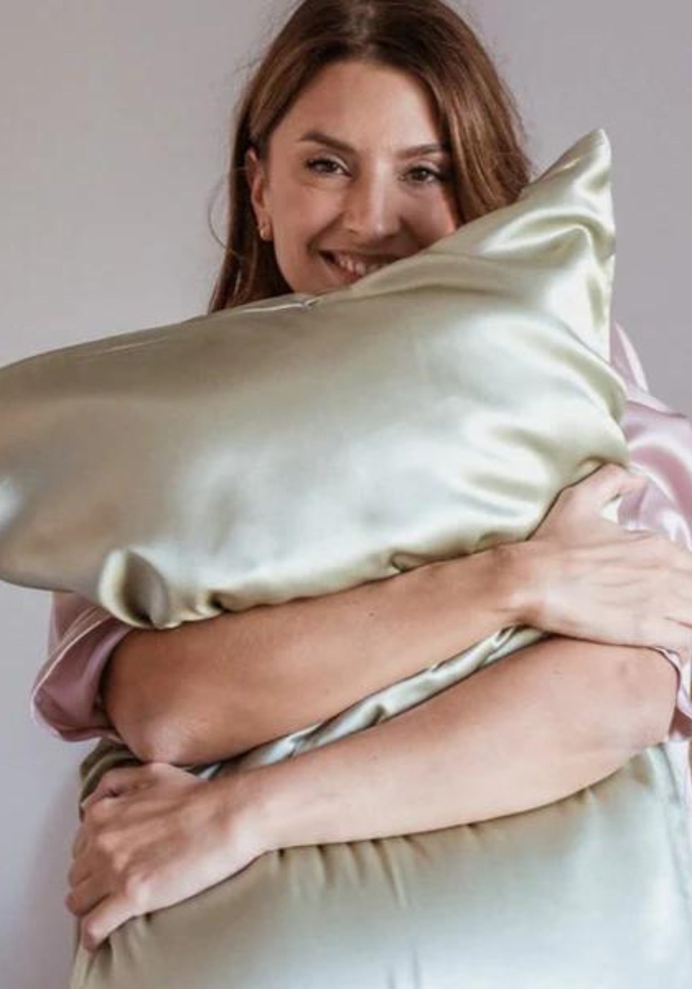 La femme tient contre elle l'oreiller avec la taie en soie vert amande de chez Emily's Pillow