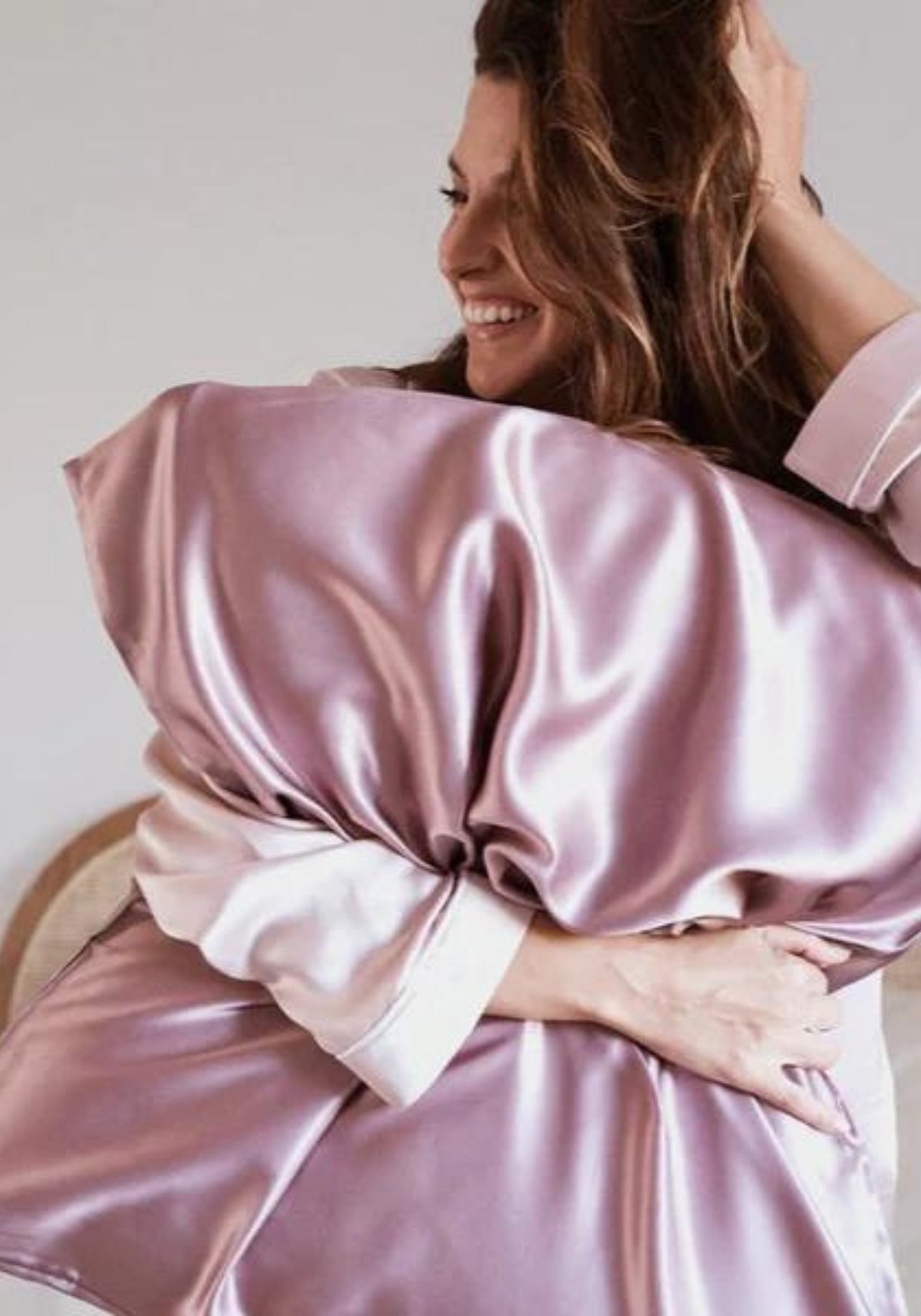 La femme tient contre elle l'oreiller avec la taie en soie vieux rose de chez Emily's Pillow
