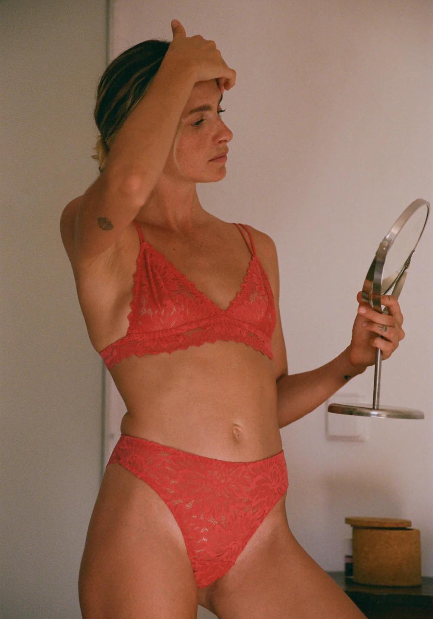 La femme se regarde dans un miroir et porte le soutien-gorge triangle Tiaki rouge lychee de chez Nénés Paris