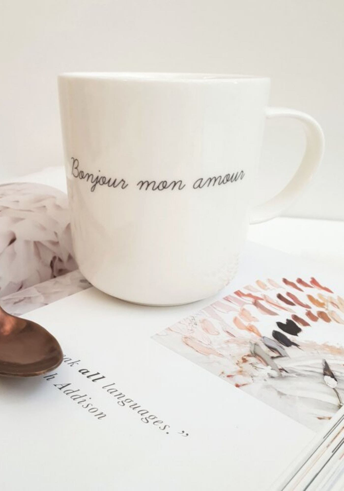 Le mug à message en faïence "Bonjour mon amour" de chez Sophie Masson est posé sur un magazine